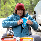 Person in outdoor setting holding a Good To-Go Cuban Style Rice pouch, with a vehicle and trees in the background