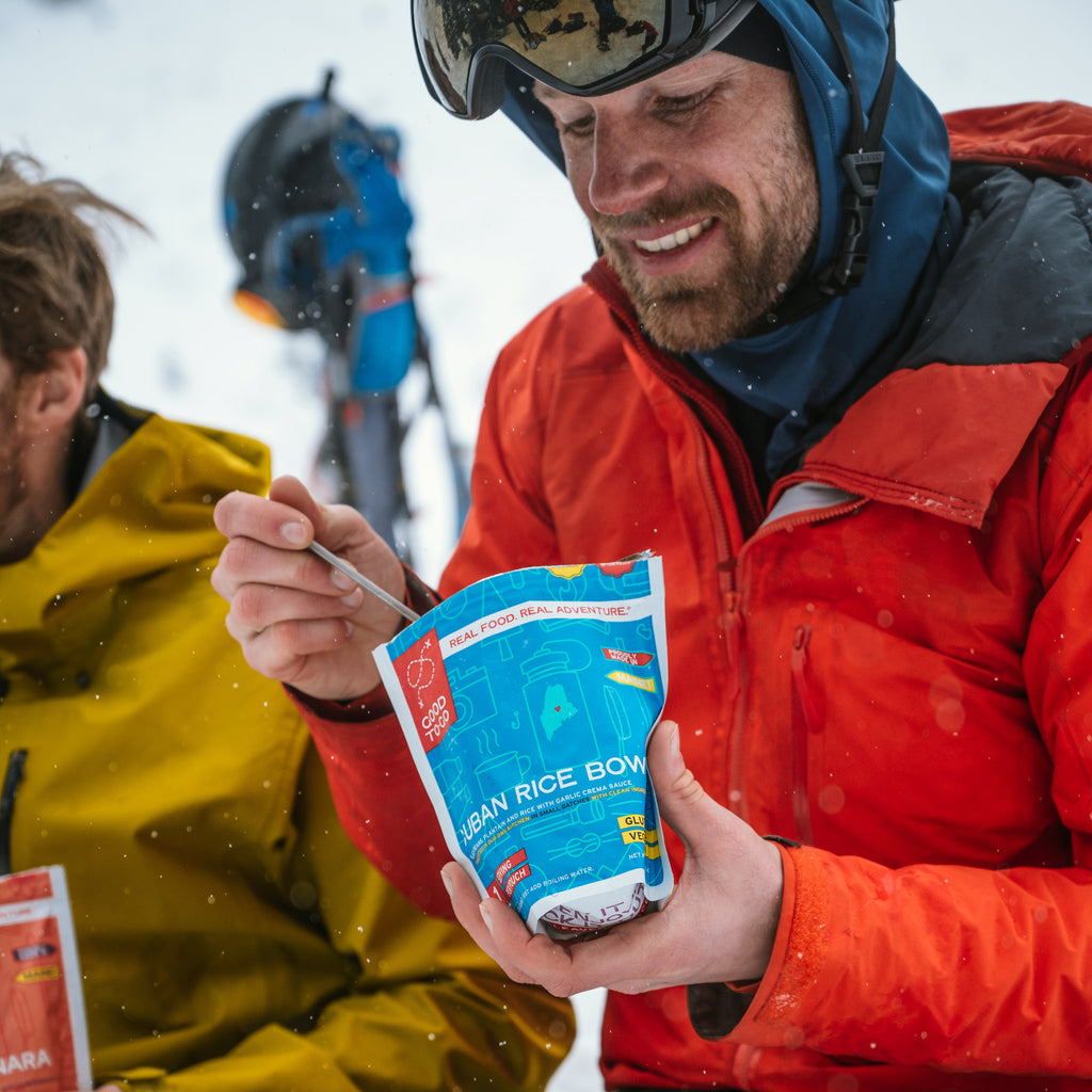 Person in red jacket eating a package of Good To-Go Cuban Style Rice in a snowy outdoor setting.