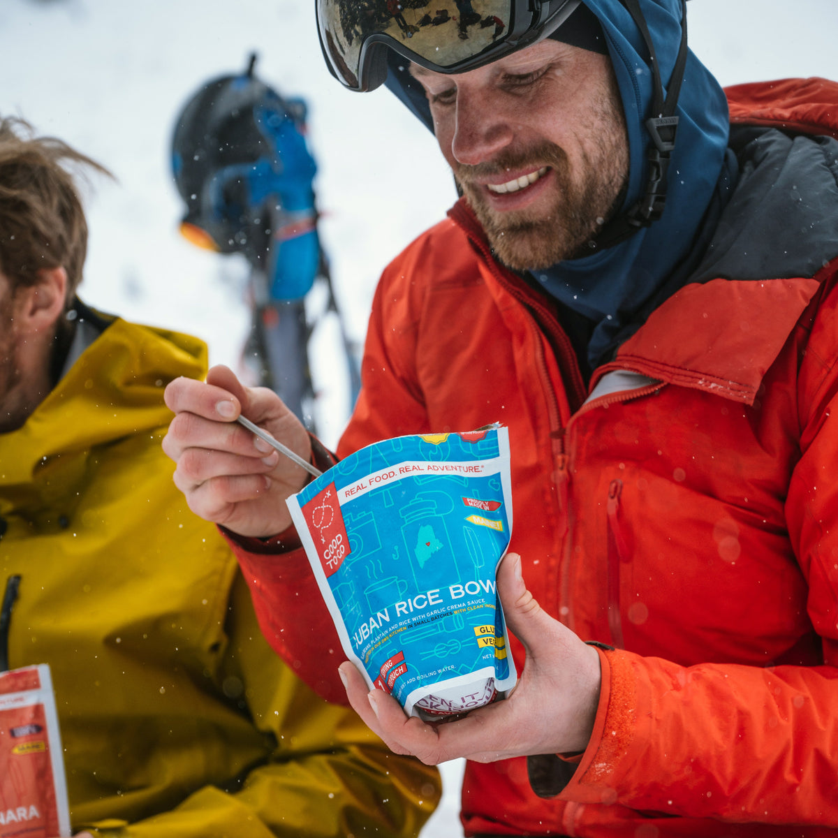 Person in red jacket eating a package of Good To-Go Cuban Style Rice in a snowy outdoor setting.