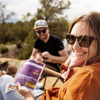 Woman holding a package of Mushroom Risotto while sitting outdoors with a man in the background.