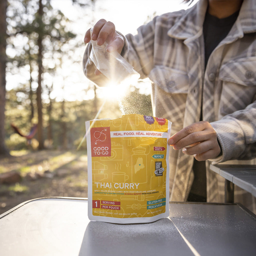 Person opening a Good To-Go Thai Curry package outdoors with trees in the background
