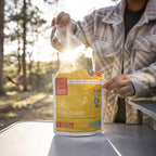 Person opening a Good To-Go Thai Curry package outdoors with trees in the background