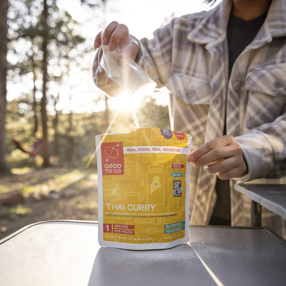 Person opening a Good To-Go Thai Curry package outdoors with trees in the background