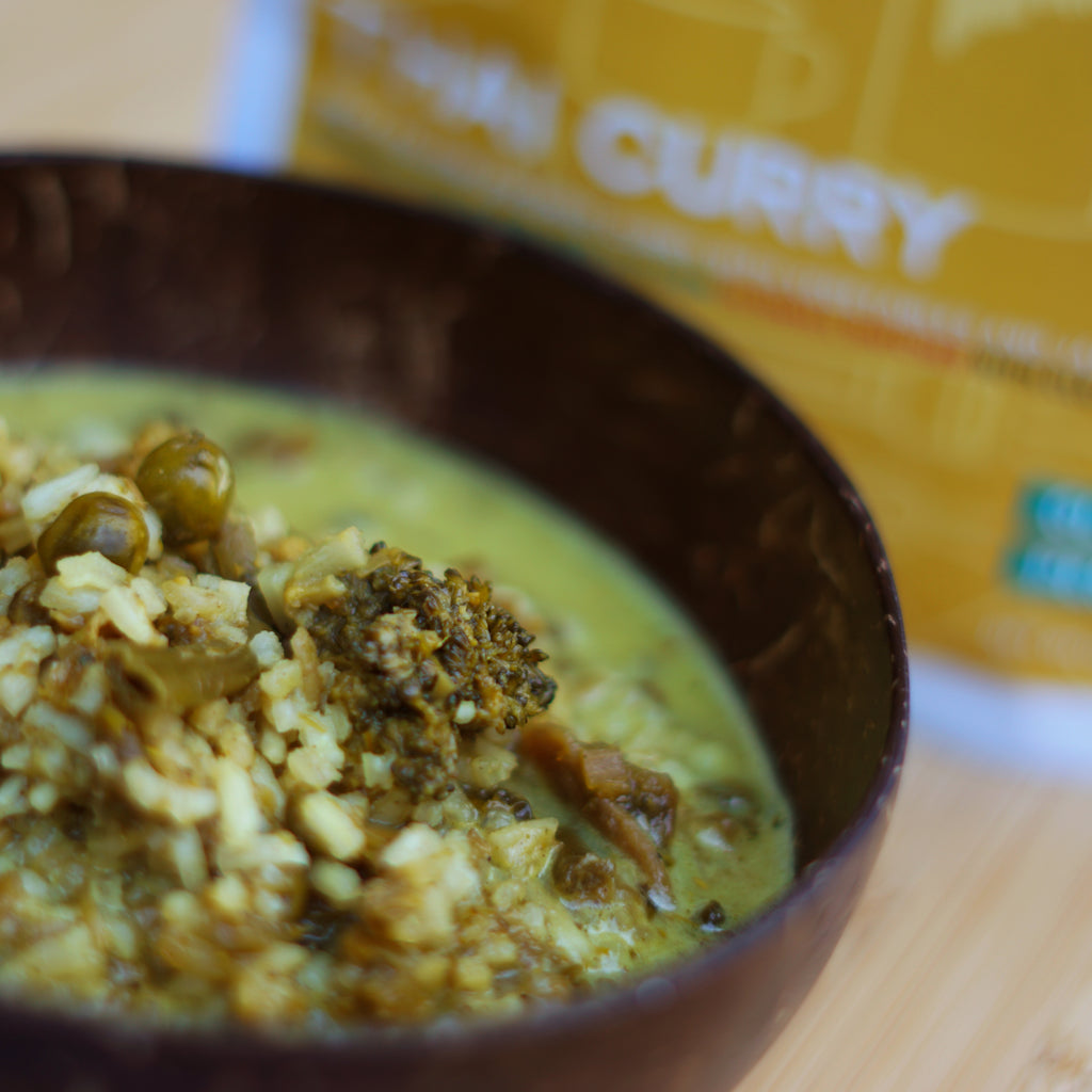 Bowl of curry with rice and peas on a wooden surface, with a pouch of curry in the background.