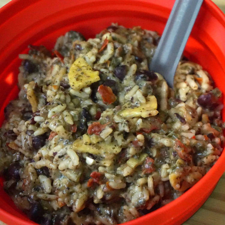 Mixed rice dish with vegetables in a red bowl with a gray spoon.